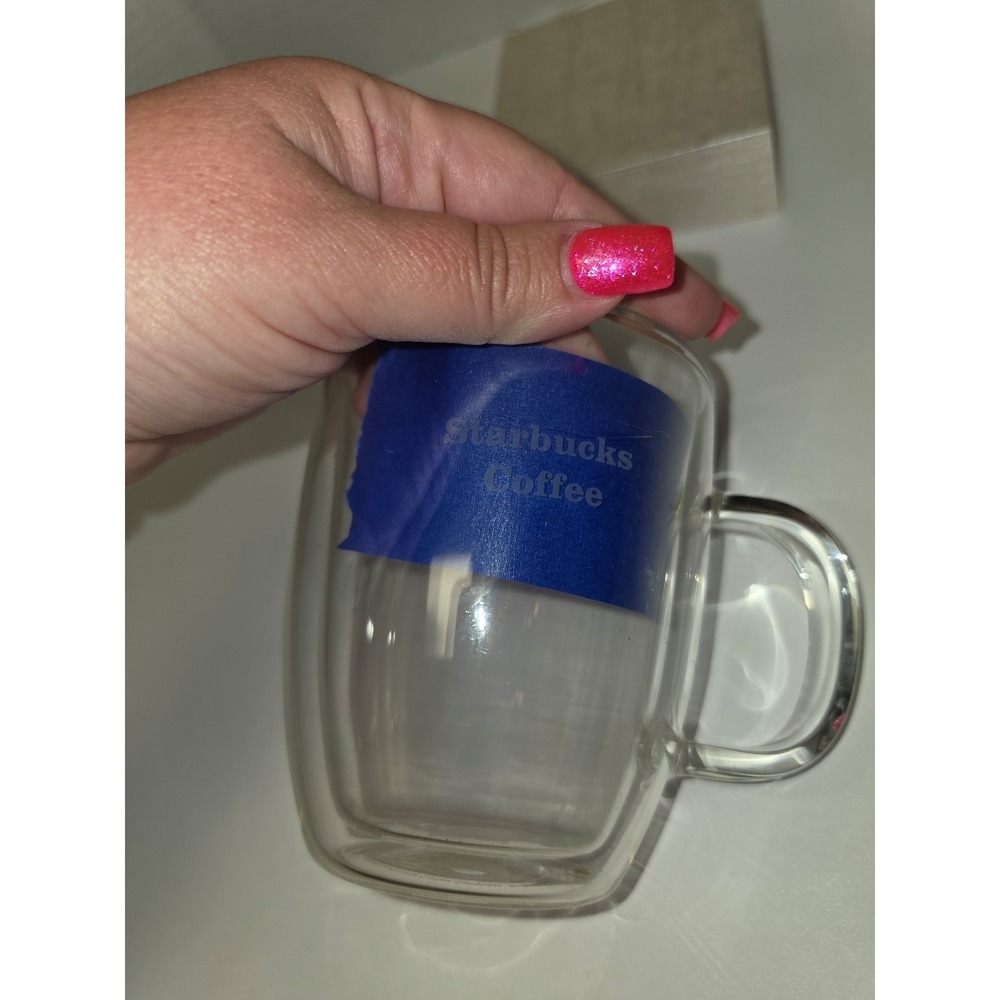 clear, double-walled glass coffee mug featuring a blue logo label and a handle.